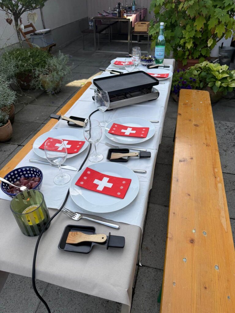 Kültéri asztal svájci zászlós szalvétákkal és raclette sütővel megterítve a közös vacsorához